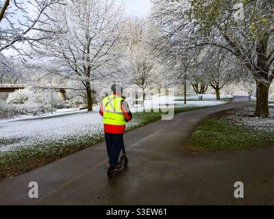 Ein Mann auf einem Motorroller in einem Park im Schnee, Ontario, Kanada. Konzepte: Winter, Spaß, Ausflug, Solo, ungewöhnlich, Balance. Frühling und Winter, zu gleichen Teilen. Jahreszeiten vermischen, überlappen, zusammengenäht. Stockfoto