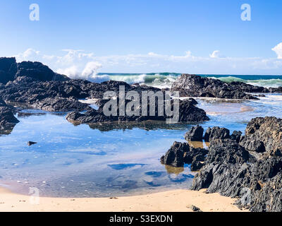 Wellen krachen gegen Felsen am Sandstrand, planschen, um die Wolken in einem blauen Himmel zu erreichen, schöner Tag, Sawtell Australien Stockfoto