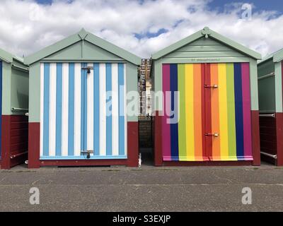 Farbenfrohe Strandhütten an der Promenade von Hove Gardens, East Sussex, Großbritannien, eine in Regenbogenfarben gestreift, die andere in den blau-weißen Streifen des Fußballclubs Brighton und Hove Albion. Stockfoto