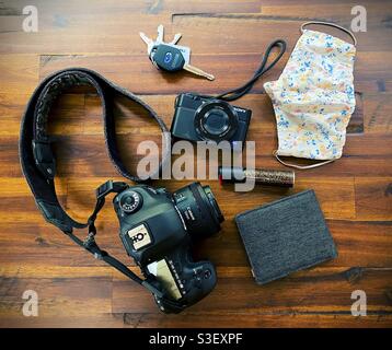 Draufsicht auf die Ausrüstung eines Straßenfotographers, darunter zwei Arten von Kameras, Schlüsseln, Gesichtsmaske, Brieftasche und Pfefferspray. Stockfoto