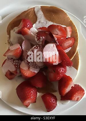 Teller mit geschnittenen Erdbeeren auf Buttermilch-Pfannkuchen mit Rahm Weiße Porzellanteller Stockfoto