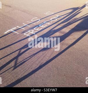 Ein Schatten eines Fahrrads mit den Worten das ist Freiheit geschrieben als Graffiti auf dem Bürgersteig auf dem Tempelhofer Feld, Berlin, Deutschland Stockfoto