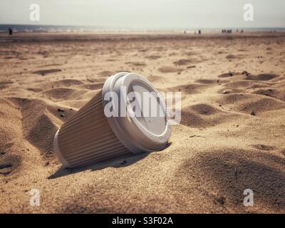 Eine weggeworfene Kaffeebecher aus Karton und Kunststoff zum einmaligen Gebrauch zum Mitnehmen Liegen an einem schönen Sandstrand in einem Umweltprobleme Konzept Stockfoto