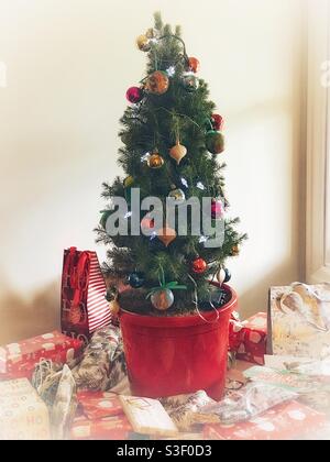 Kleiner geschmückter Weihnachtsbaum ein roter Topf, umgeben von Geschenken Bei hellem Morgensonnenlicht Stockfoto