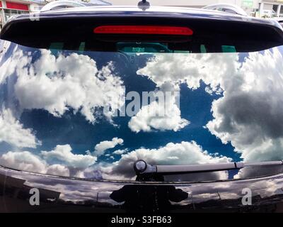 Sommerzeit. Cumulus-Wolken spiegeln sich in der Heckscheibe eines SUV wider. Konzeptionell: Einladung, zu fliegen, zu träumen, zu reisen, abzuheben, Fernweh, los Stockfoto