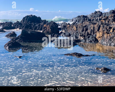 Glänzendes, glasig aussehendes Meerwasser mit kleinen Schaumstoffflecken oben in den Felsenpools am Strand, Sawtell Australia Stockfoto