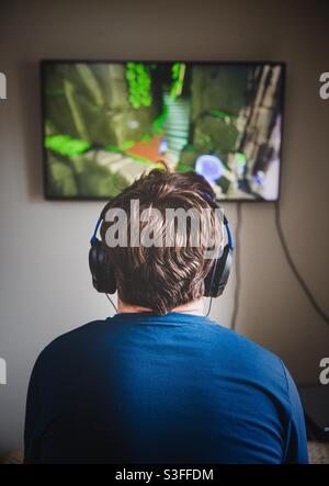 Rückansicht eines Teenagers, der allein in seinem Schlafzimmer sitzt Videospiele spielen und einen fernsehbildschirm ansehen Stockfoto