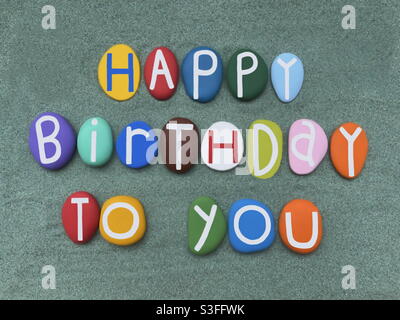 Alles gute zum Geburtstag, kreative Textkomposition mit mehrfarbigen handgemalten Steinbuchstaben über grünem Sand Stockfoto