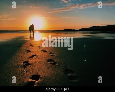 Fußabdrücke auf dem Sand, die zu einem Paar vor dem Hotel führen Eines wunderschönen Sonnenuntergangs Stockfoto