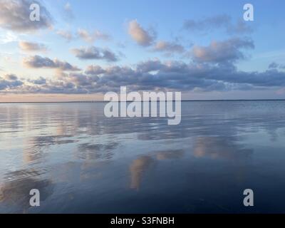 Pastellfarbene Sonnenwolken spiegeln sich auf dem noch immer in der Bucht verlaufendem Wasser Stockfoto