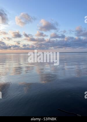 Der Himmel bei pastellfarbenem Sonnenuntergang und Wolken spiegeln sich auf dem noch immer in der Bucht abgehenden Wasser Stockfoto