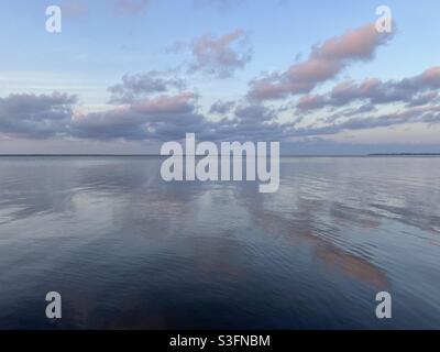 Sanfte Abendwolken bei Sonnenuntergang und Himmel, die sich auf das ruhige Bay Water spiegeln Stockfoto