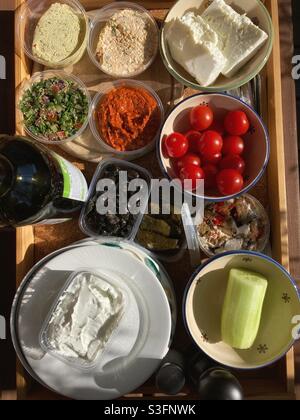 Eine Auswahl an verschiedenen frischen Dips, Oliven, Käse, Tomaten und Gurken in Kunststoff- und Porzellanschüsseln auf einem Tablett Stockfoto