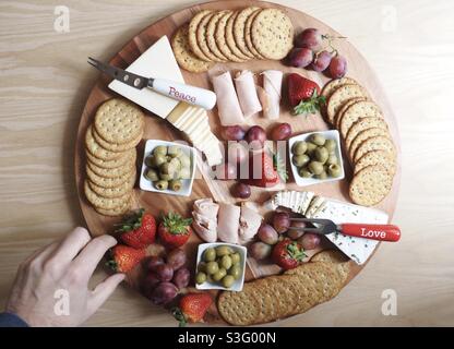 Essen, männliche Hand, die nach Erdbeeren greift, sind kein Wurstbrett, frischer Käse, Oliven, Cracker Stockfoto