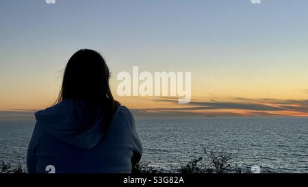 Blick von hinten, eine Frau mit Silhouetten, die in der Dämmerung über den Pazifik blickt Stockfoto