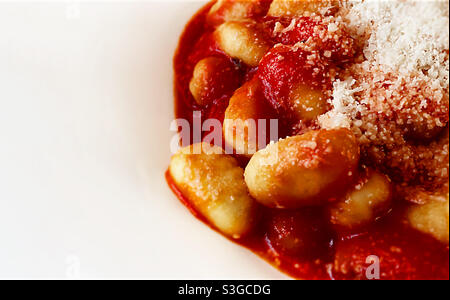 Nahaufnahme einer Portion Gnocchi in Tomatensauce mit geriebenem Parmesankäse, serviert auf einer weißen Keramikplatte. Italienische Küche und Küche. Stockfoto