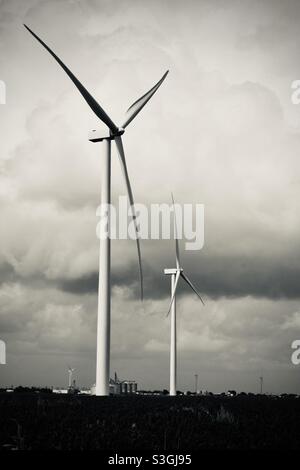 Schwarz-weißes Bild von zwei Windturbinen auf einem Feld gegen einen bewölkten Himmel Stockfoto