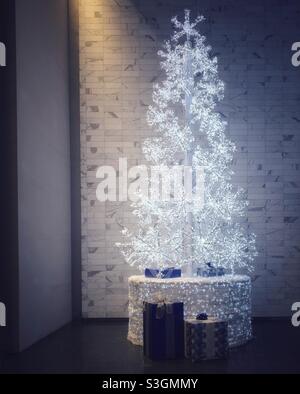 Weißer Weihnachtsbaum, der eine dunkle Ecke eines Foyer-Büroblocks im Zentrum von Calgary, Alberta, Kanada, beleuchtet. Stockfoto