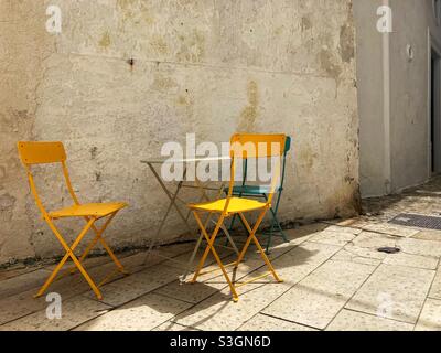 Ein kleiner Bistrotisch und drei Stühle in der Straße vor einem Café in Vieste, Apulien, Italien Stockfoto