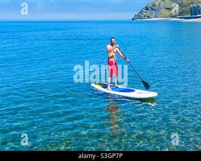 Aberystwyth, West Wales, Großbritannien. Freitag, 16. Juli 2021. Ein Mann paddelt an einem heißen Sommertag am Aberystywth-Strand im Juli. Bildnachweis ©️ Rose Voon / Alamy Live News. Stockfoto