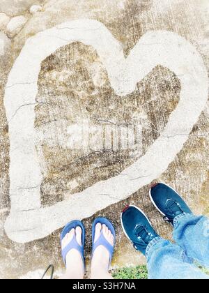Mann und Frau Füße zusammen in der Nähe eines gemalten Herzens. Selfie eines verliebten Paares. Valentinstag-Jubiläumskonzept. Stockfoto