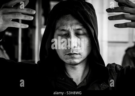 Mann, der vor der chinesischen Botschaft stand, mit geschlossenen Augen und erhobenen Händen in der Luft und bete. Er protestiert gegen die Verfolgung und den Völkermord an den Uiguren durch China. Stockfoto