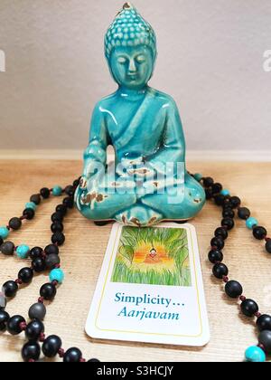 Eine Buddha-Figur, Gebetsperlen und eine umgedrehte Dharma-Karte mit dem Wort „Einfachheit“. Stockfoto