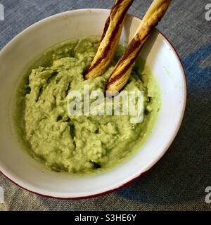 Hausgemachtes Avocado-Dip in Schüssel mit Brotstangen. Stockfoto