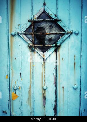 Alte, verwitterte blaue Tür mit Diamantfenster. Stockfoto