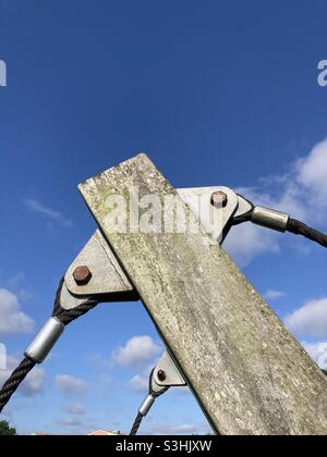 Vor dem blauen Himmel sind Seile an einem grau verwitterten Holzbalken mit Metallösen und Bolzen befestigt Stockfoto