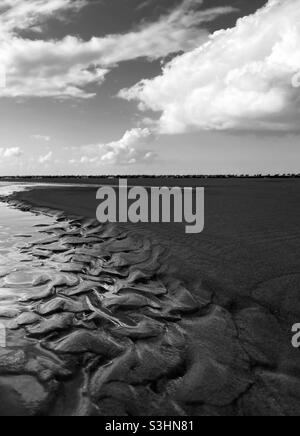 Muster, die durch Wind und Wellen im Sand am Strand mit Wolken am Himmel entstehen Stockfoto