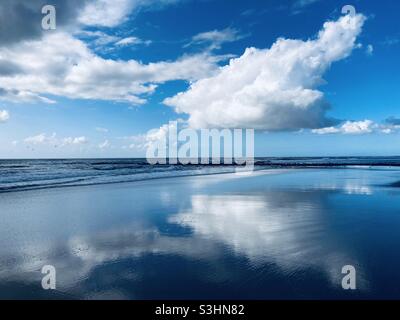 Eine leuchtend weiße Wolke am blauen Himmel spiegelt sich auf der glatten Wasseroberfläche des Meeres wider Stockfoto