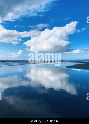 Eine leuchtend weiße Wolke am blauen Himmel spiegelt sich auf der glatten Wasseroberfläche des Meeres wider Stockfoto