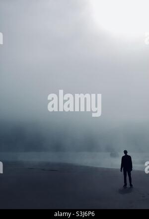 Mann stand an einem nebligen Strand und blickte aufs Meer Stockfoto