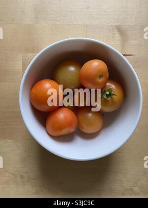 Minimalistisches Stillleben Bild von hausgemachten frisch gepflückten Tomaten in einer weißen Porzellanschale auf einem hellen Kiefernholztisch Stockfoto