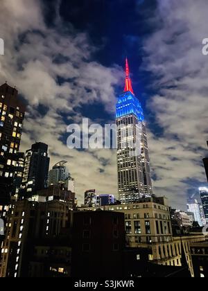 Das Empire State Building mit rot-weißen und blauen Lichtern vor einem bewölkten Nachthimmel Stockfoto