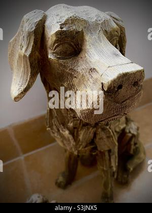 Handgeschnitzte Holzstatue eines labrador-Welpen, der auf einem gefliesten Innenboden sitzt Stockfoto