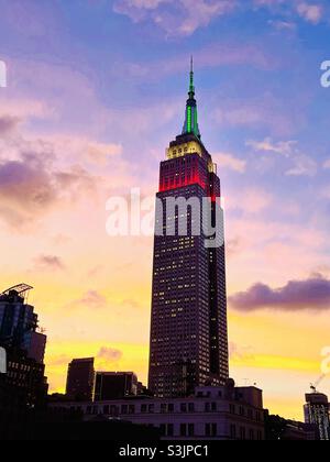 Die grün-weißen und roten Turmlichter des Empire State Building leuchten vor einem farbenfrohen Sonnenuntergang in Midtown Manhattan, New York City, USA Stockfoto