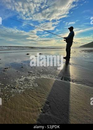 Schattenangler an einem walisischen Strand bei Sonnenuntergang Stockfoto