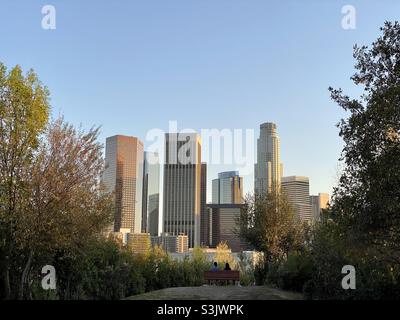 LOS ANGELES, CA, 2021. JANUAR: Skyline der Innenstadt mit Wolkenkratzern vom Park im Norden der Stadt aus gesehen, wurden die Menschen auf einer Bank im Vordergrund silhouettiert Stockfoto
