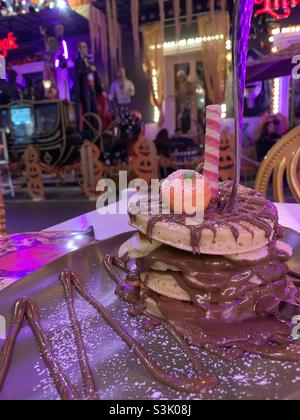 Stapel von Pfannkuchen mit Schokoladensauce bedeckt mit Halloween-Figuren im Hintergrund Stockfoto