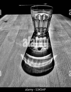 Ein Glas Wasser steht auf einem Holztisch und wirft einen langen Schatten Stockfoto