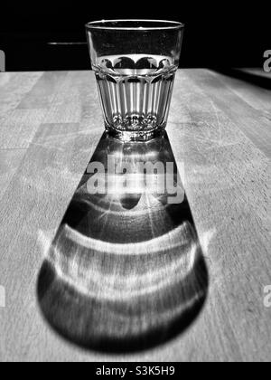 Ein Glas Wasser steht auf einem Holztisch und wirft einen langen Schatten Stockfoto