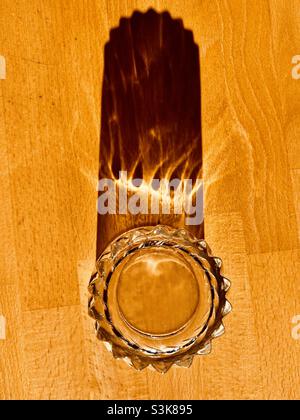 Ein Glas Wasser steht auf einem Holztisch und wirft einen langen Schatten Stockfoto