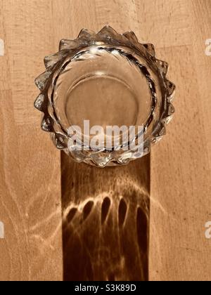 Ein Glas Wasser steht auf einem Holztisch und wirft einen langen Schatten Stockfoto