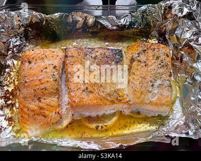 Nahaufnahme von gebratenen Lachsfilets auf einem Bett aus geschnittenen Zitronen in Aluminiumfolie. Stockfoto