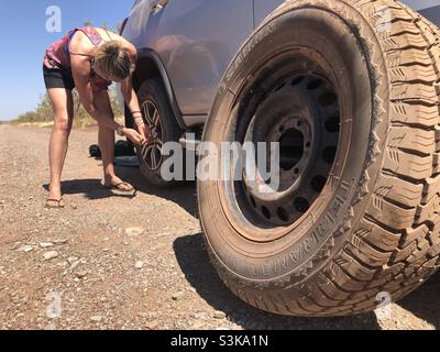 Eine Frau wechselt auf einer staubigen Outback-Straße in Westaustralien einen Reifen Stockfoto