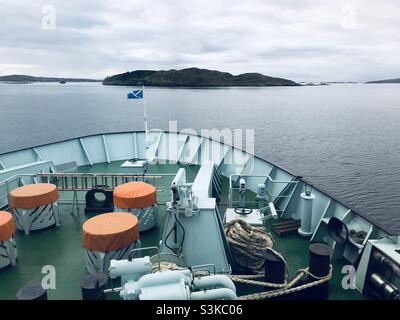 Der Bug eines Schiffes mit der schottischen Flagge, die im Wind fliegt, und einer kleinen Insel voraus Stockfoto