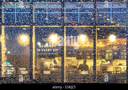 Blick durch eine mit Regentropfen bedeckte Windschutzscheibe in den warmen Glanz eines Cafés. Calgary, Alberta, Kanada. Stockfoto