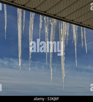Eiszapfen, die von einem Balkon hängen und vor einem blauen Himmel hervorgehoben sind. Stockfoto